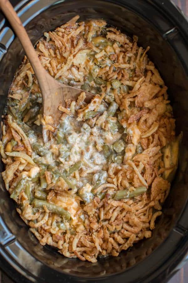 **Gratin di Fagiolini al Formaggio a Cottura Lenta** 2 Casseruola di fagiolini al formaggio, cremosa e appena cotta, nella pentola lenta, con un cucchiaio che serve una porzione abbondante.