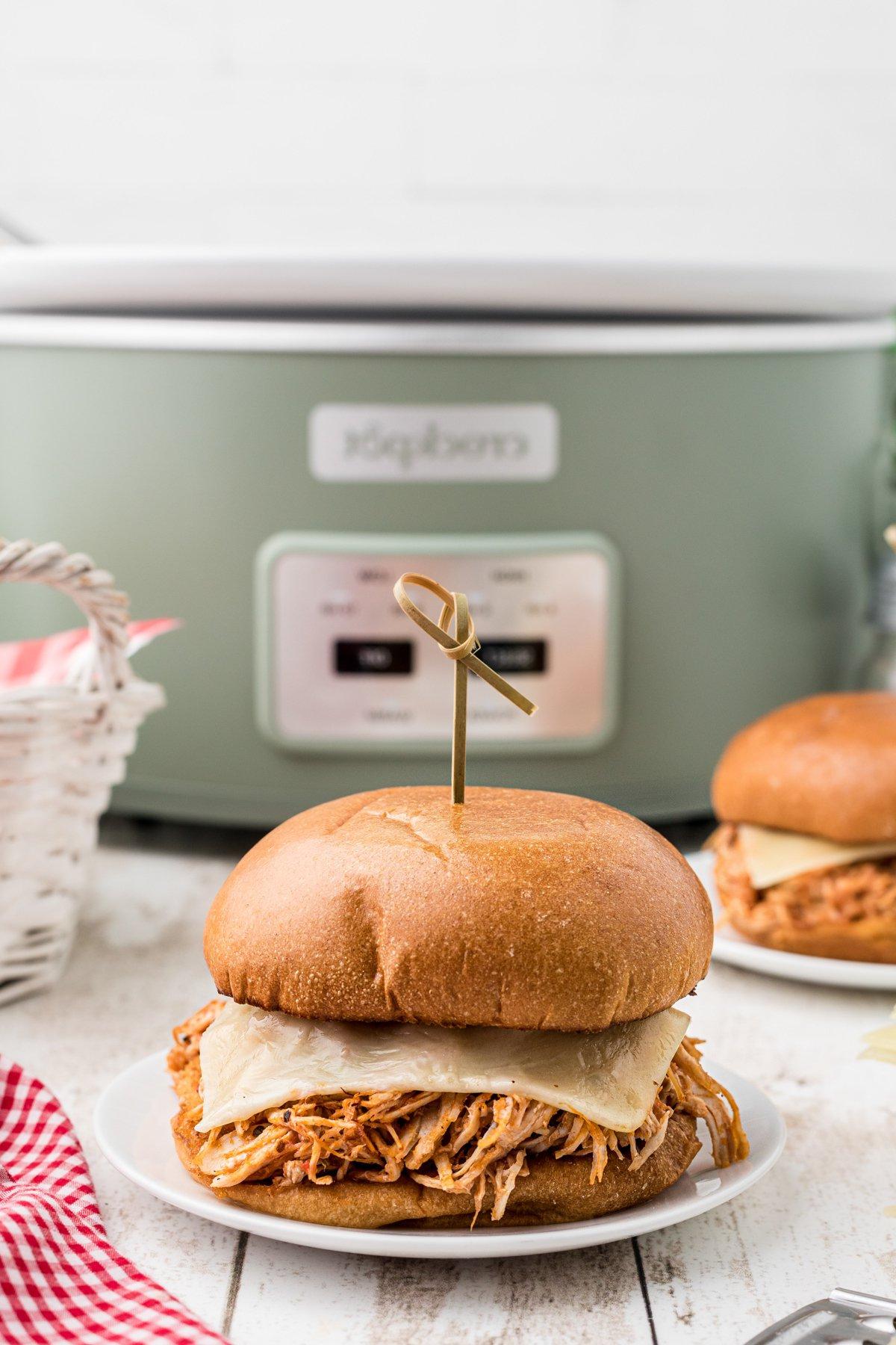 Panini al Pollo alla Parmigiana a Cottura Lenta 2 Un panino di pollo alla parmigiana in primo piano con una slow cooker sullo sfondo.