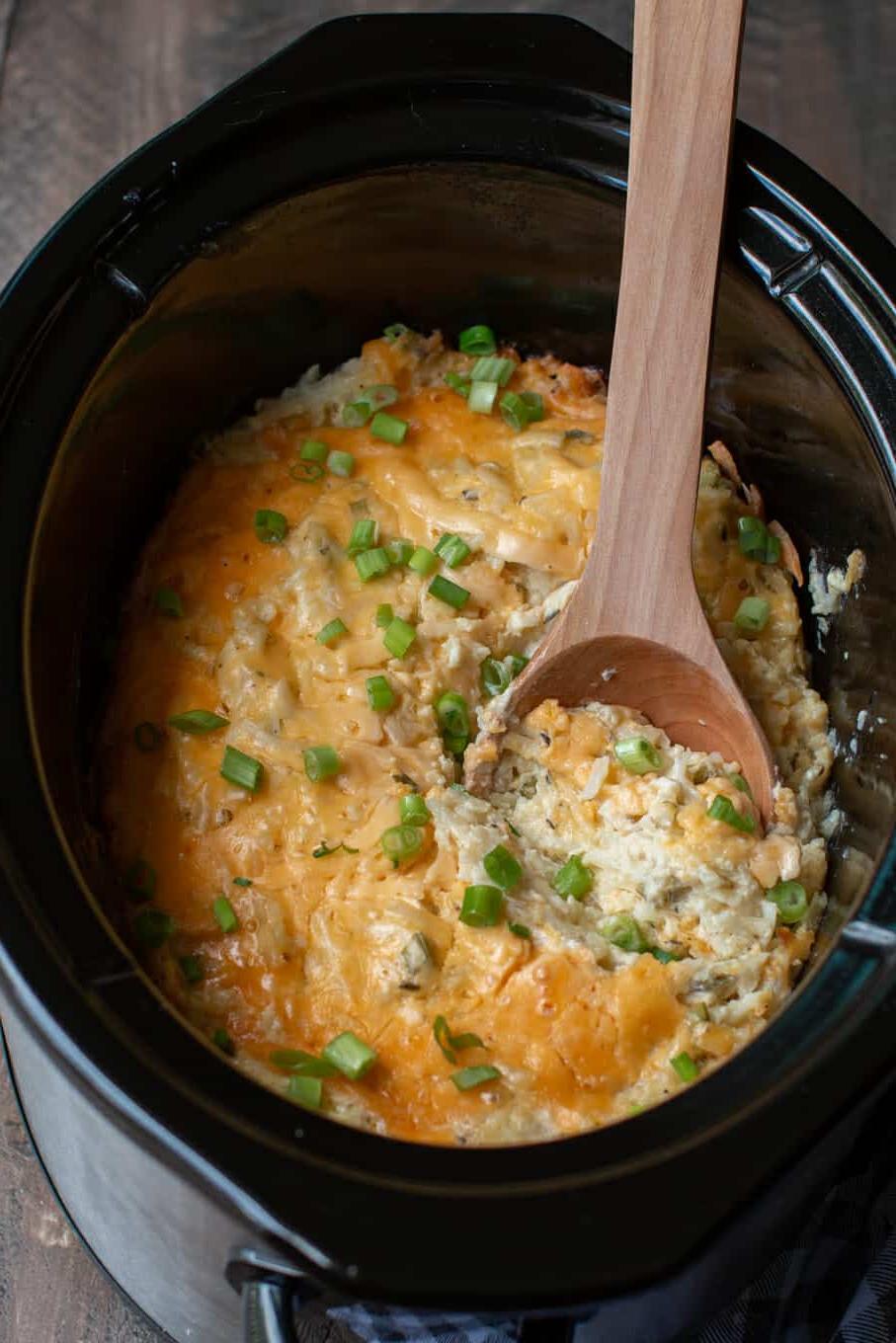 Patate per Feste in Slow Cooker 2 Patate al formaggio nella slow cooker con un cucchiaio di legno che raccoglie una porzione.