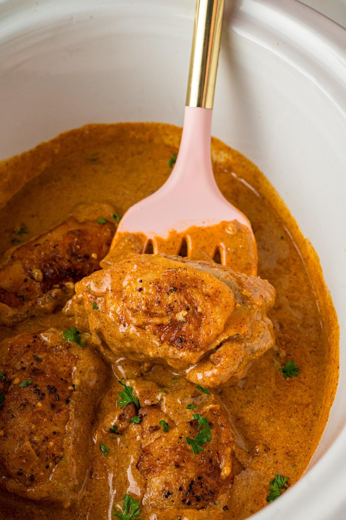 Pollo alla Paprica in Cottura Lenta 2 Una spatola che solleva un pezzo di pollo alla paprika cotto in slow cooker.