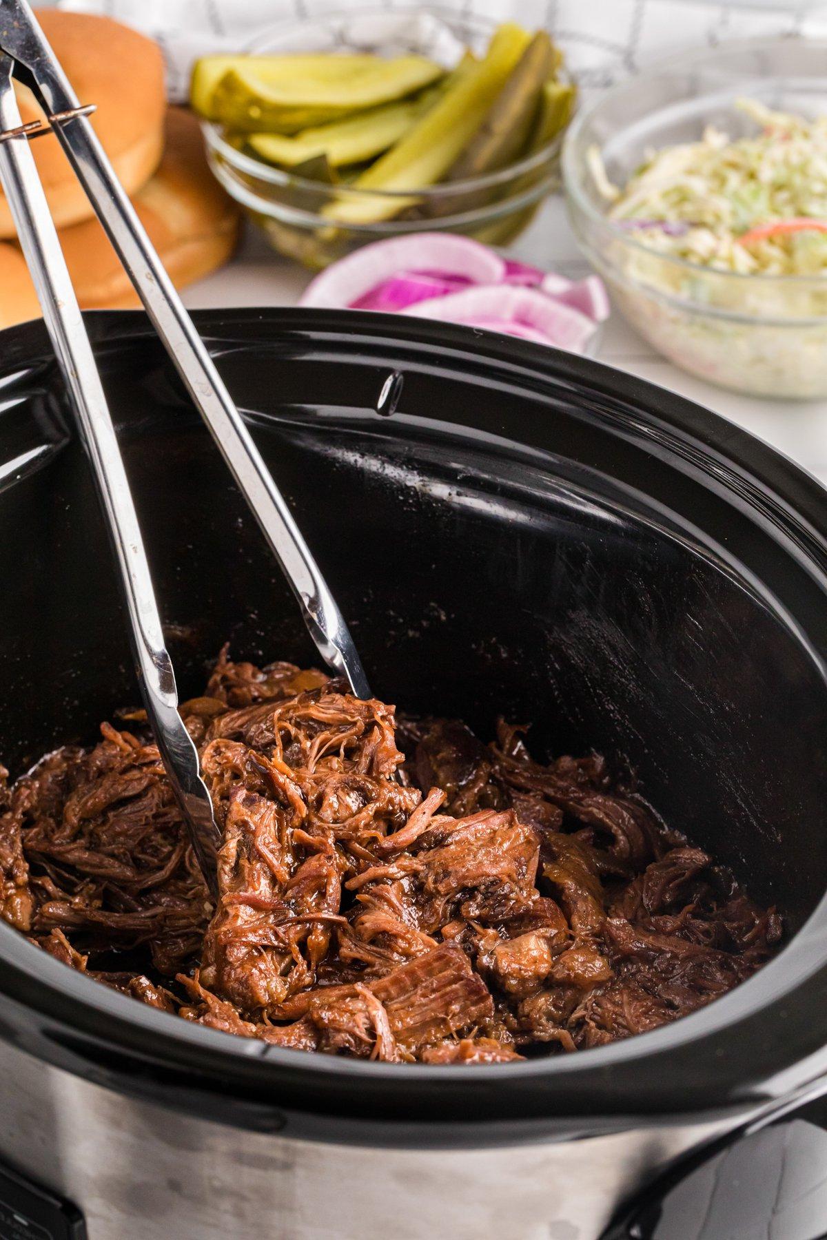 Manzo al Barbecue a Lenta Cottura 2 Manzo BBQ afferrato con pinze in una slow cooker.