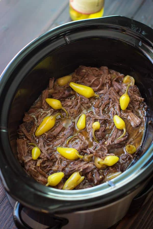 **Brasato Piccante alla Mississippi per Slow Cooker** 2 Carne sfilacciata in una slow cooker con peperoni piccanti sopra.