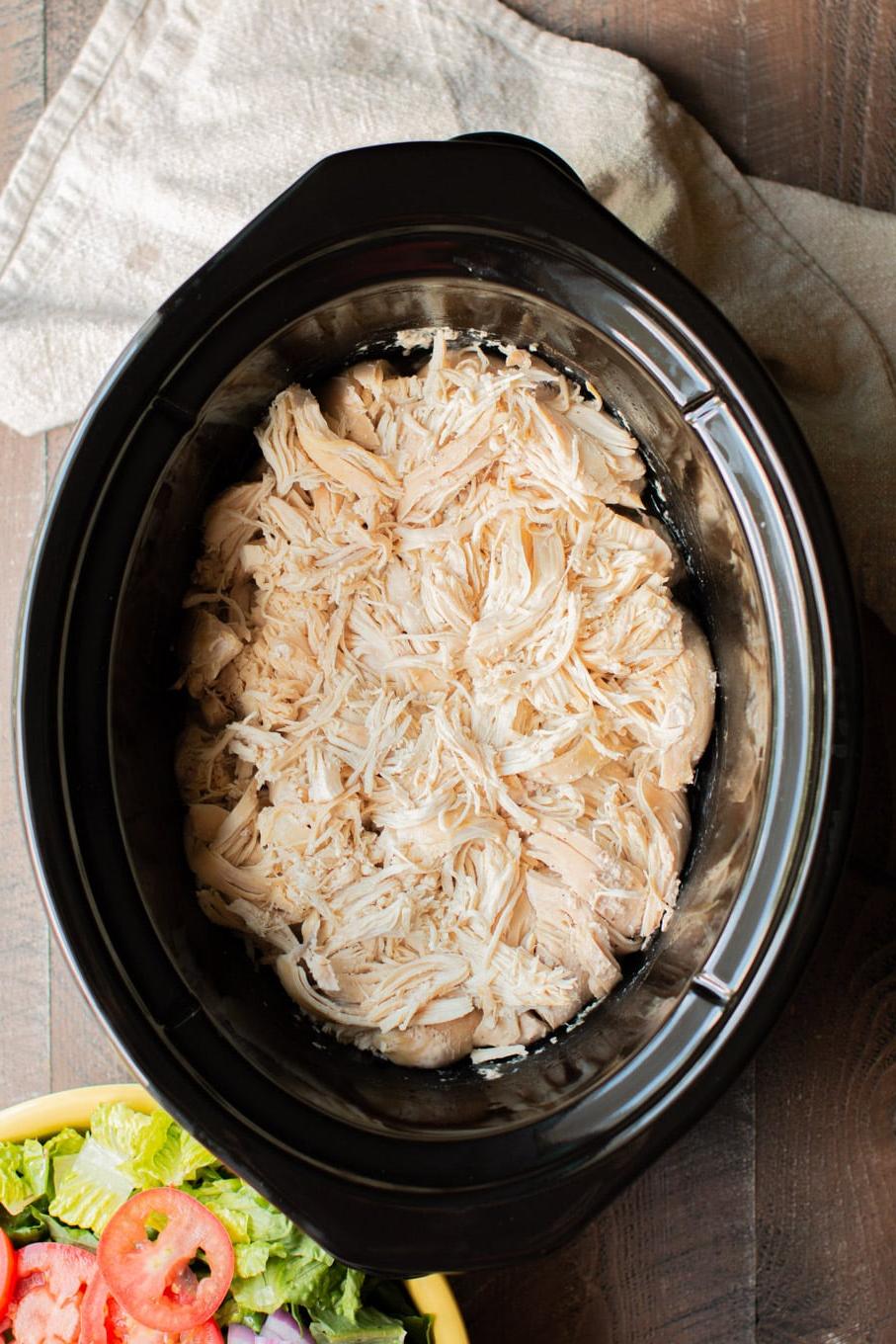 Pollo sfilacciato in slow cooker 2 pollo sfilacciato nella pentola a cottura lenta con un'insalata verde di contorno.