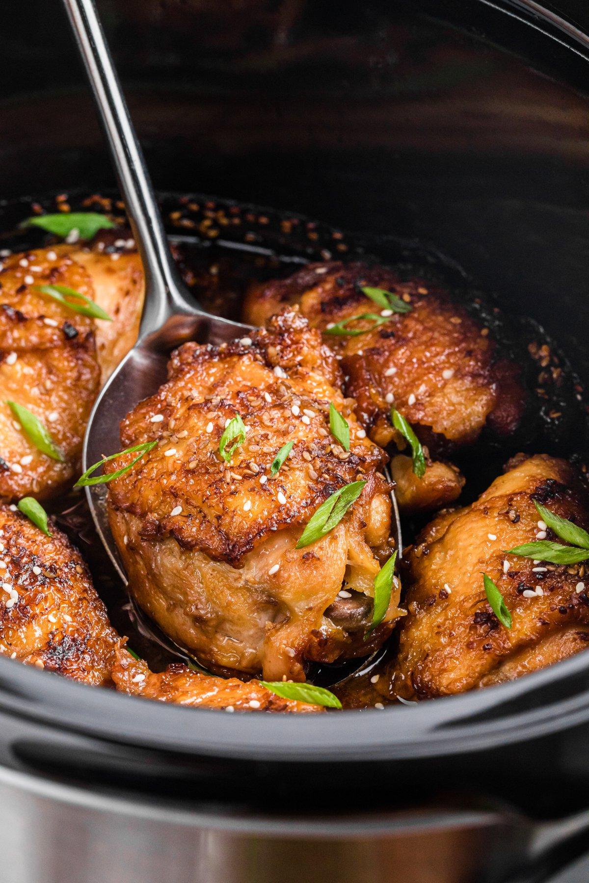 **Cosce di Pollo Teriyaki a Cottura Lenta** 2 Un cucchiaio prende una delle cosce di pollo teriyaki dalla slow cooker.