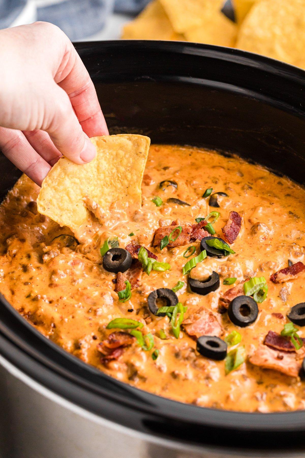 **Dip di Nachos Ricco Cotto Lentamente** 2 scooping loaded nacho dip with a tortilla chip from a slow cooker.