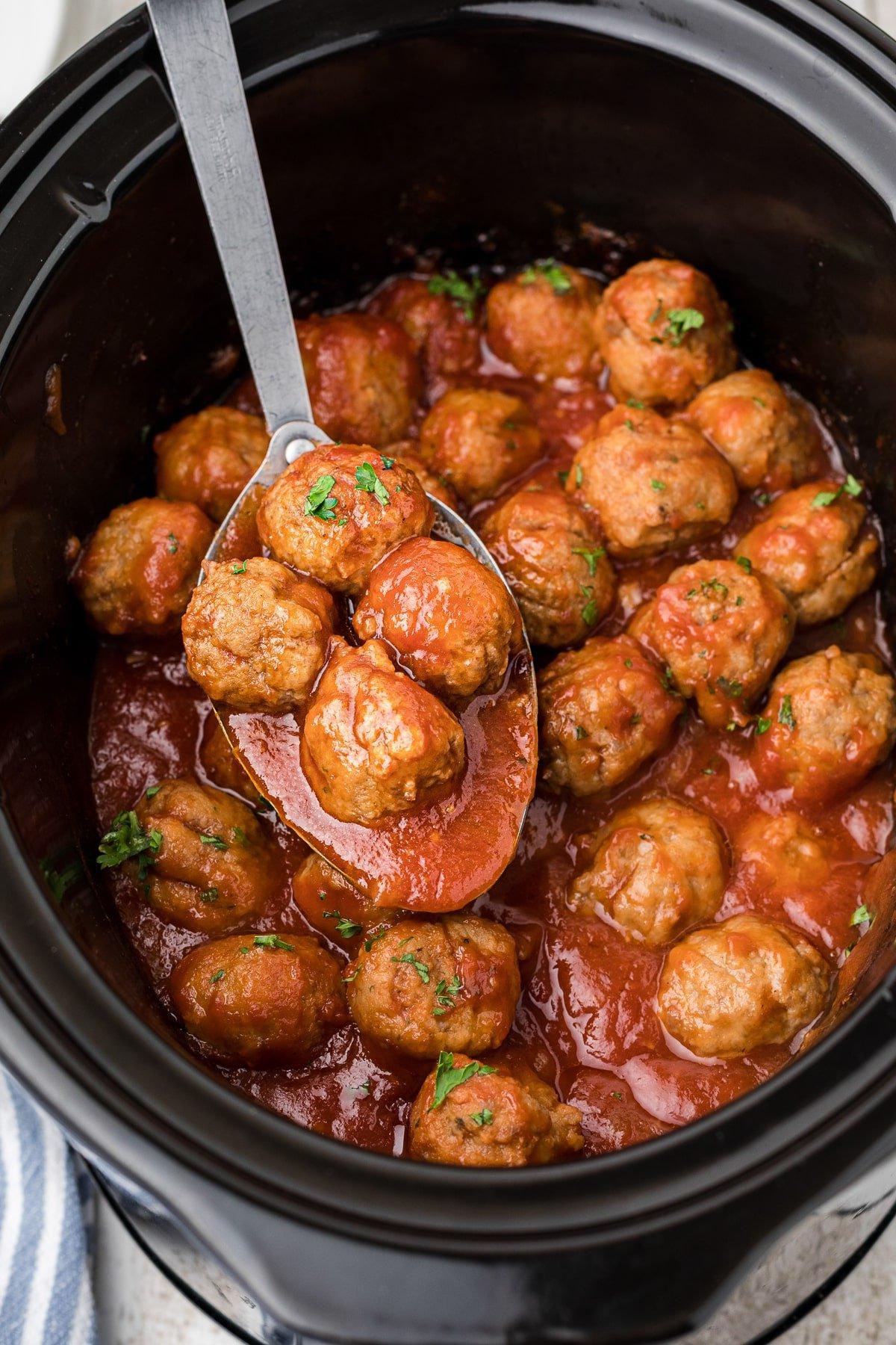 Polpette alla Birra a Cottura Lenta 2 Polpette alla birra su un cucchiaio in una slow cooker.