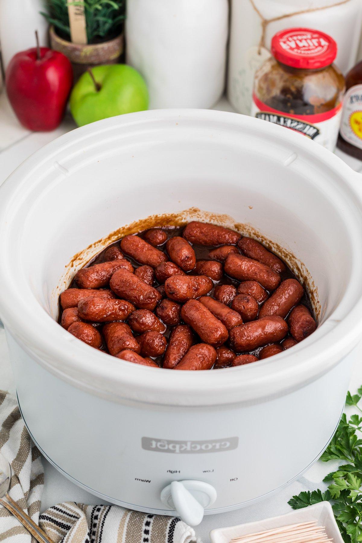 **Wurstel Piccoli al Burro di Mele in Slow Cooker** 2 Salsiccine mini al burro di mele nella slow cooker bianca, pronte per essere servite.