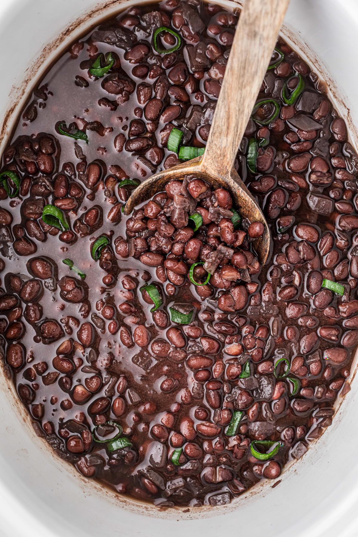 Fagioli Neri Cottura Lenta 2 Fagioli neri fumanti in una slow cooker con un cucchiaio di legno inserito.