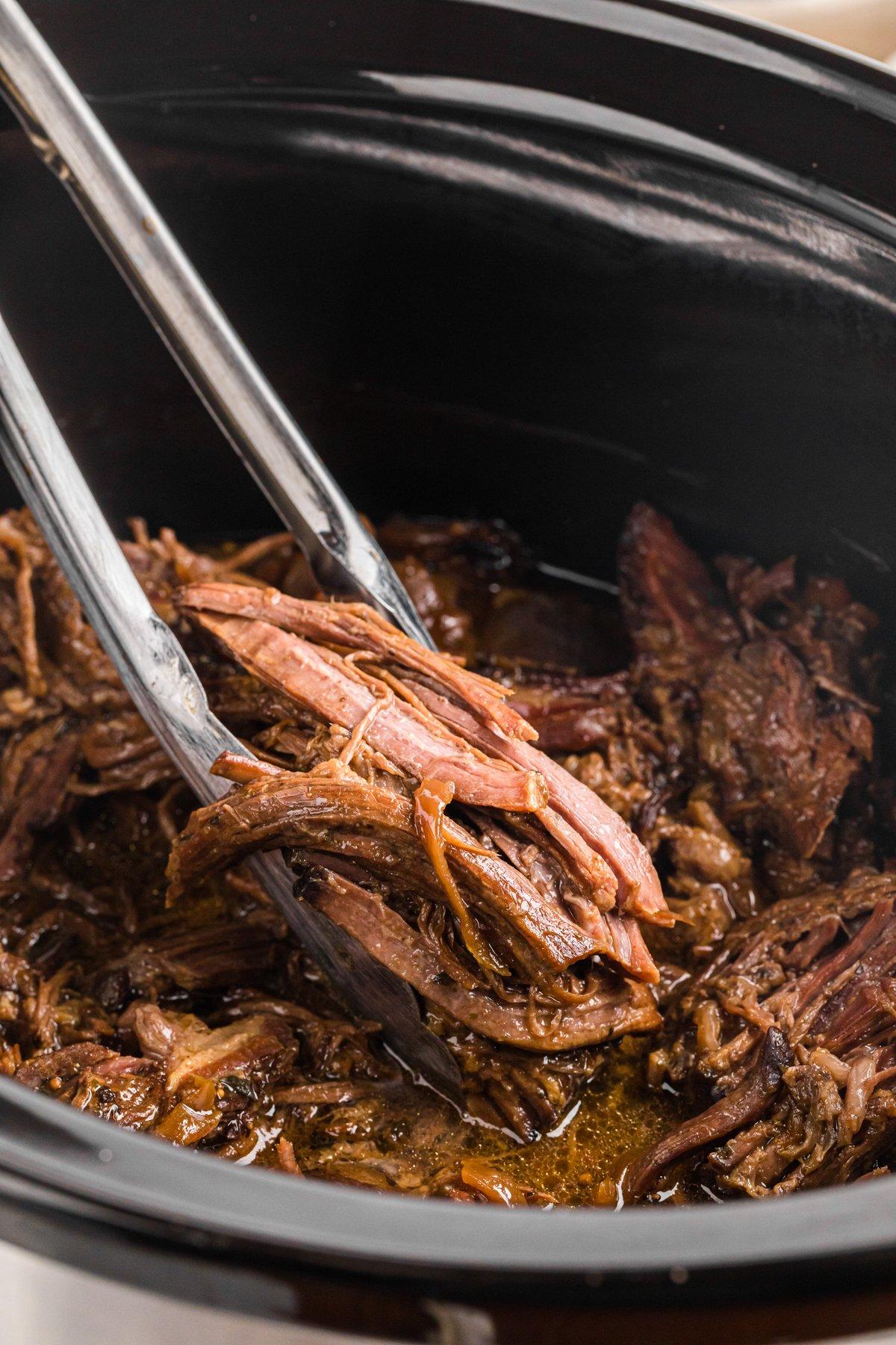 Pinze che afferrano dell'arrosto di manzo della Georgia cotto in slow cooker.