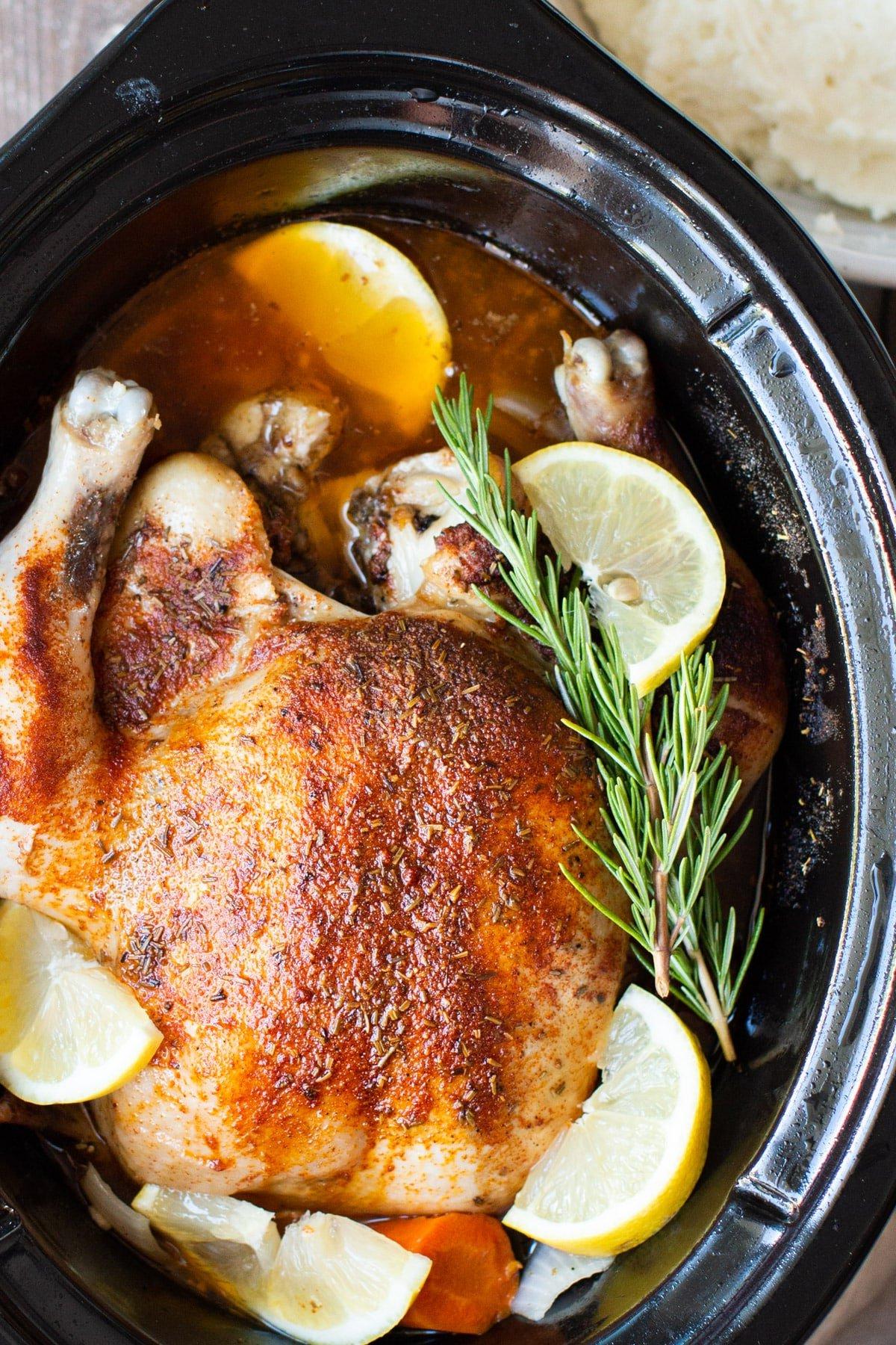 Pollo Intero in Slow Cooker 2 Primo piano di un pollo intero cotto con limone e rosmarino in una slow cooker.