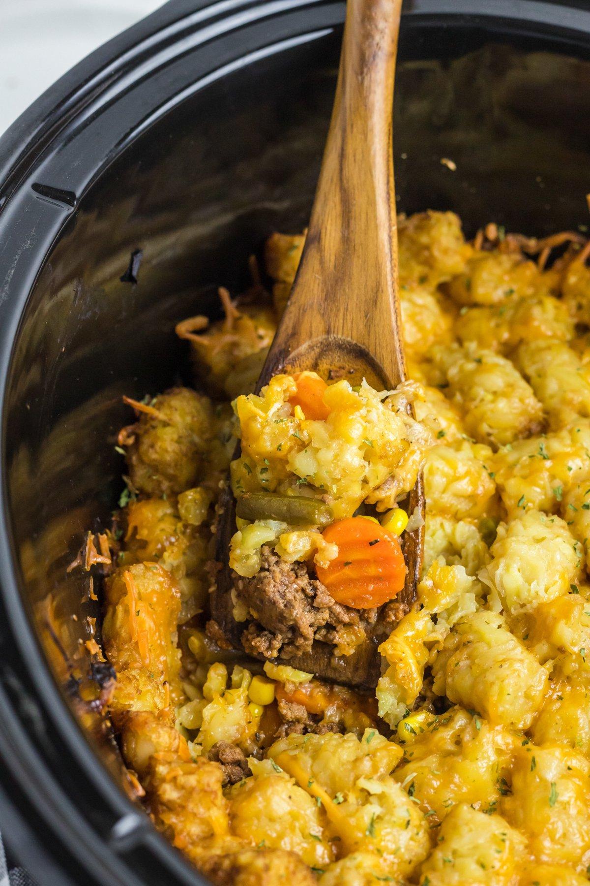 Sformato di Tater Tot alla Pastore 2 shepherd's pie in a slow cooker with a spoon in it.