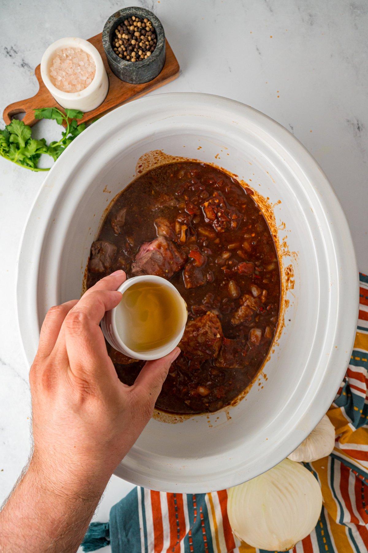 Aceto di sidro di mele aggiunto agli ingredienti in una pentola Crock-Pot.