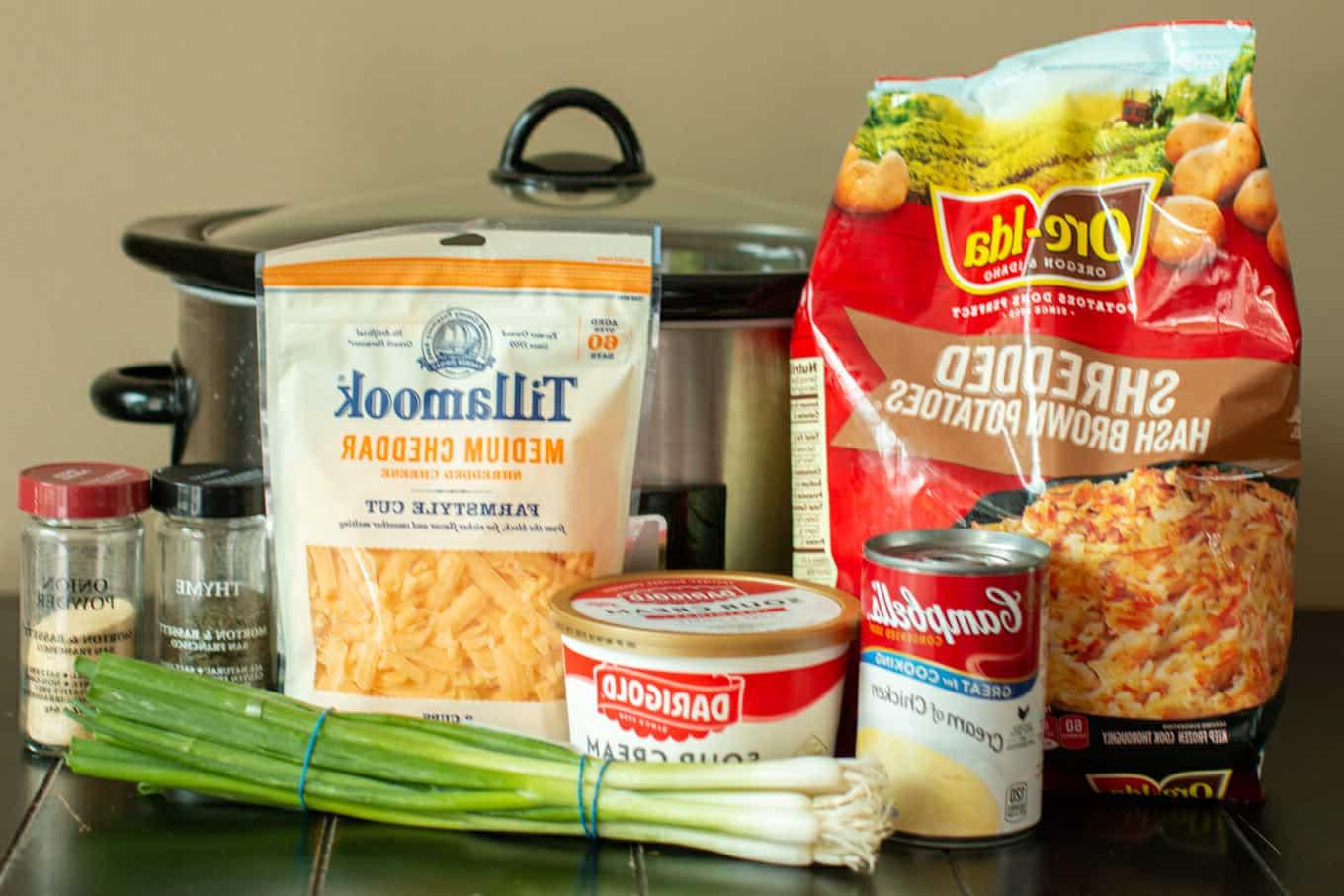 Patate per Feste in Slow Cooker 3 Ingredienti disposti: patate hash brown, panna acida, crema di zuppa di pollo, formaggio cheddar grattugiato e cipollotti freschi.