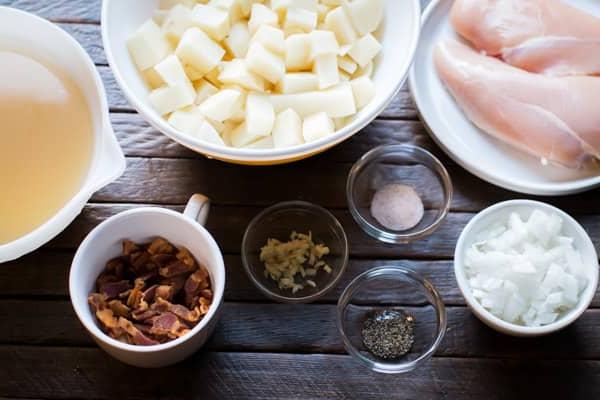 Zuppa Ricca di Pollo, Bacon e Patate in Slow Cooker 3 Petti di pollo, patate, pancetta, cipolla e condimenti su un tavolo di legno.