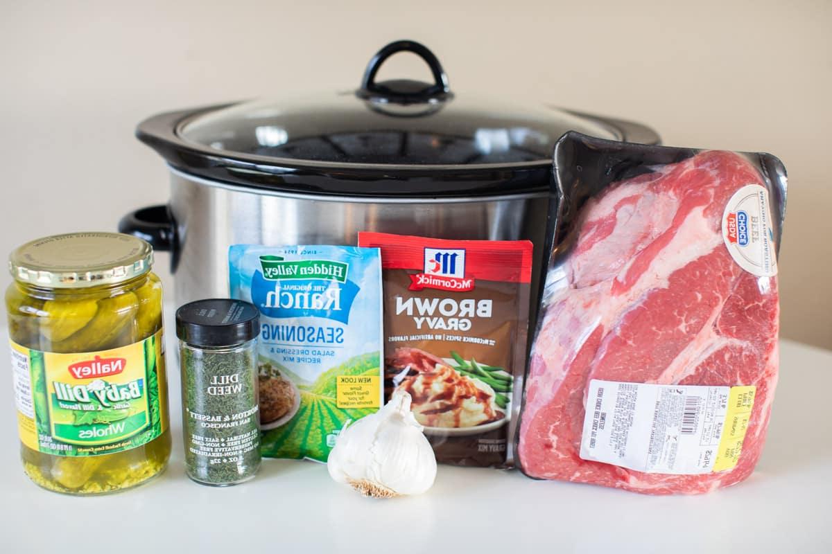 Ingredienti per il brasato di manzo ai cetriolini e aneto disposti davanti a una slow cooker.