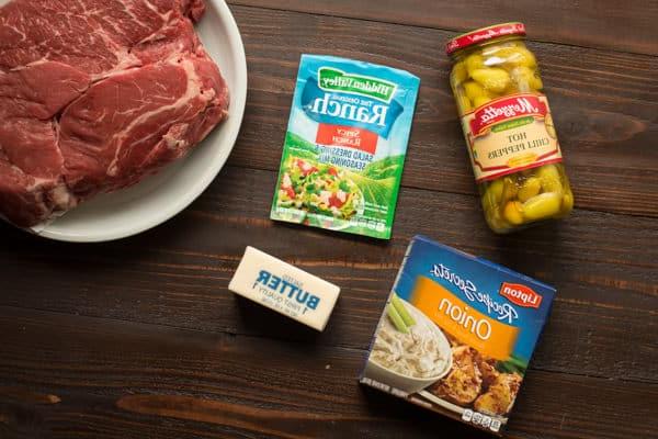 **Brasato Piccante alla Mississippi per Slow Cooker** 3 Punta di petto di manzo, ranch piccante, mix di zuppa di cipolle, peperoncini piccanti e burro su un tavolo di legno.
