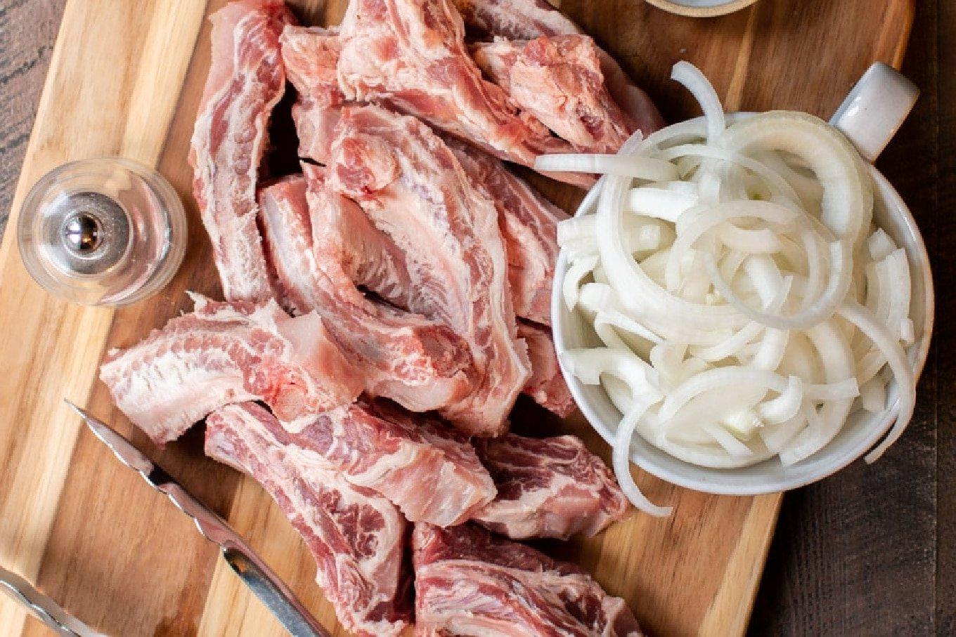 Costine, Patate e Crauti Cotte Lentamente 3 Costine e cipolle fresche su tagliere prima della cottura.