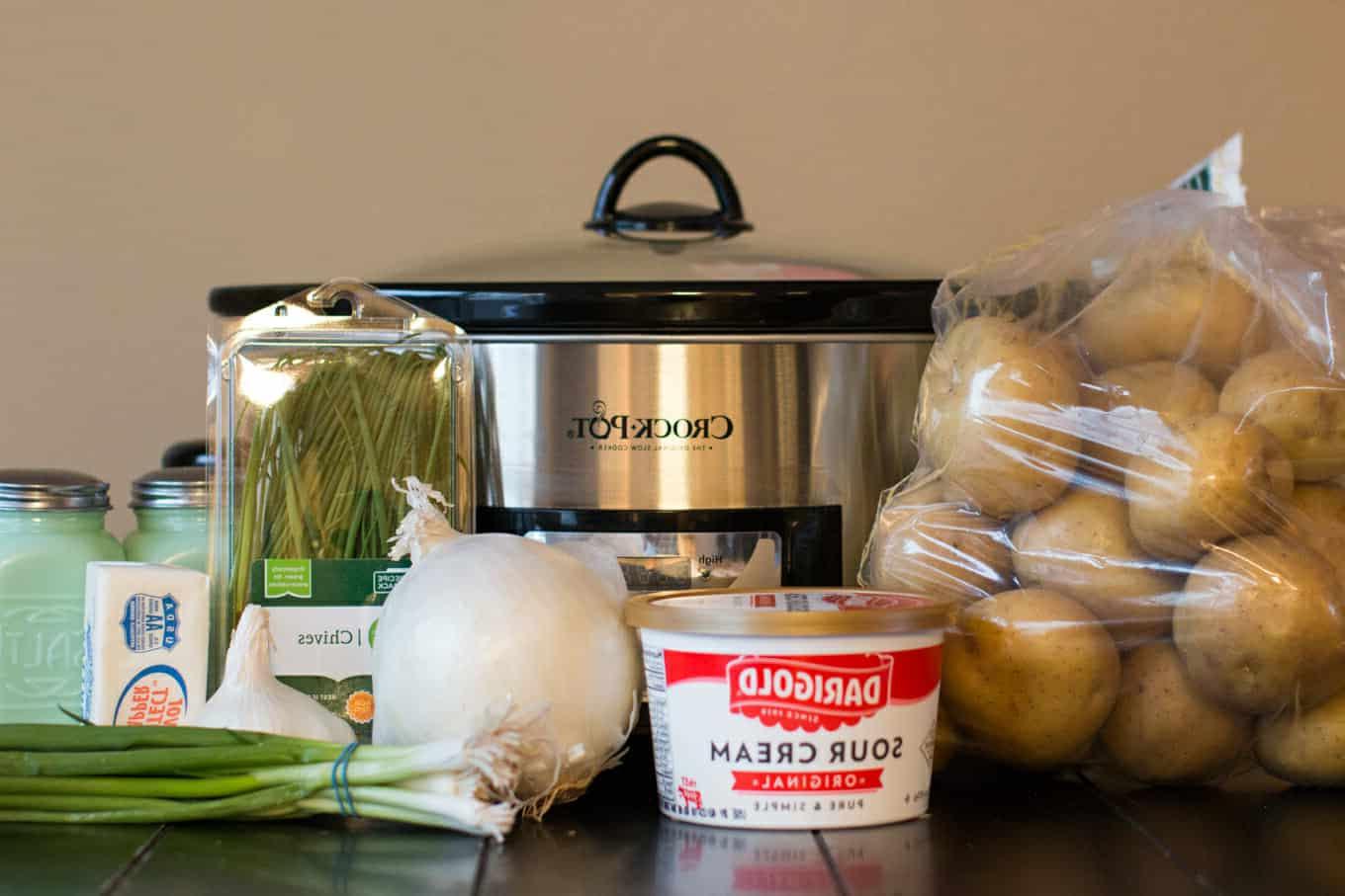 Purè di patate a cottura lenta con panna acida e cipolla 3 Ingredienti per le patate in purea: patate, panna acida, cipolla, erba cipollina e cipollina verde davanti alla slow cooker.