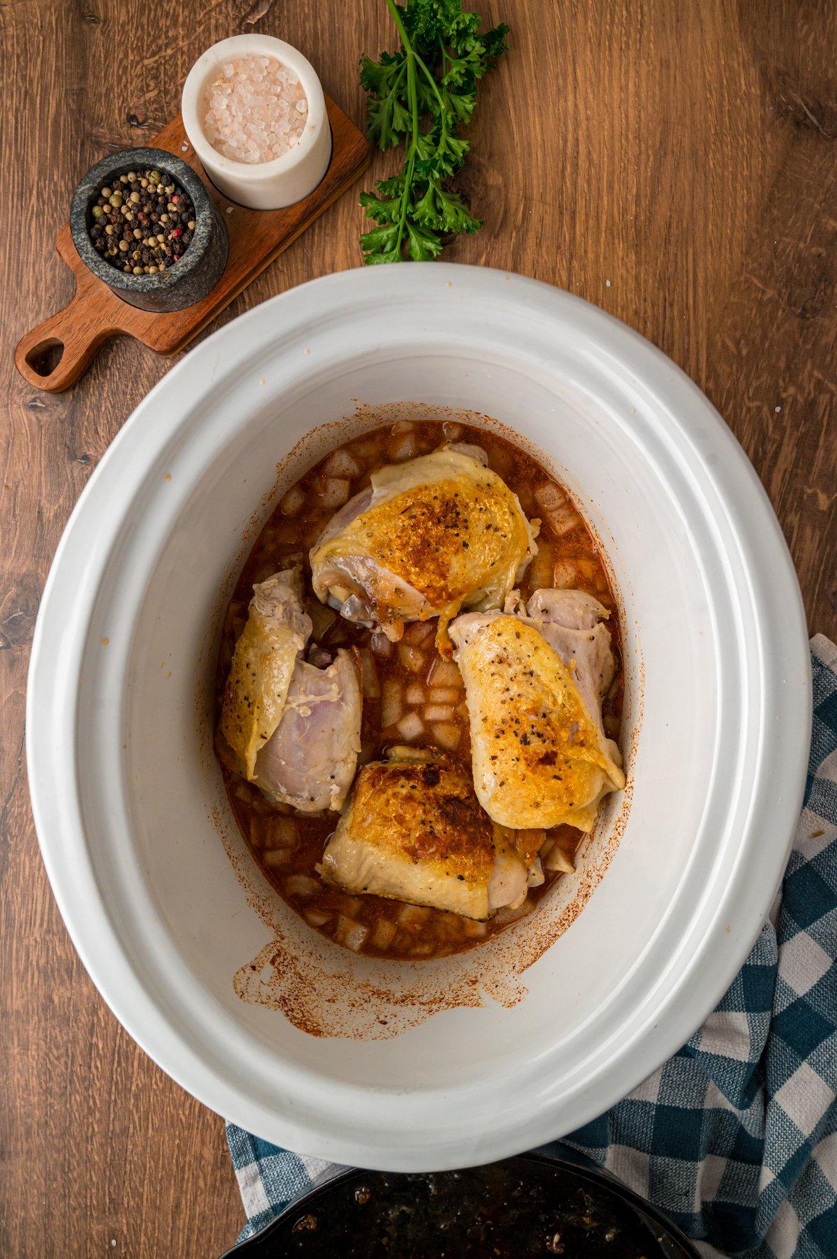 Pollo alla Paprica in Cottura Lenta 4 Cosce di pollo rosolate sopra una miscela di brodo in una crockpot.