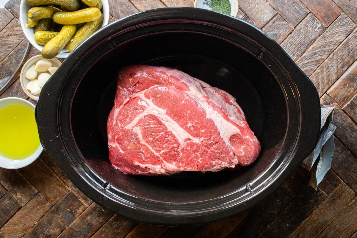 Spalla di manzo cruda posizionata all'interno di una slow cooker, pronta per gli altri ingredienti.