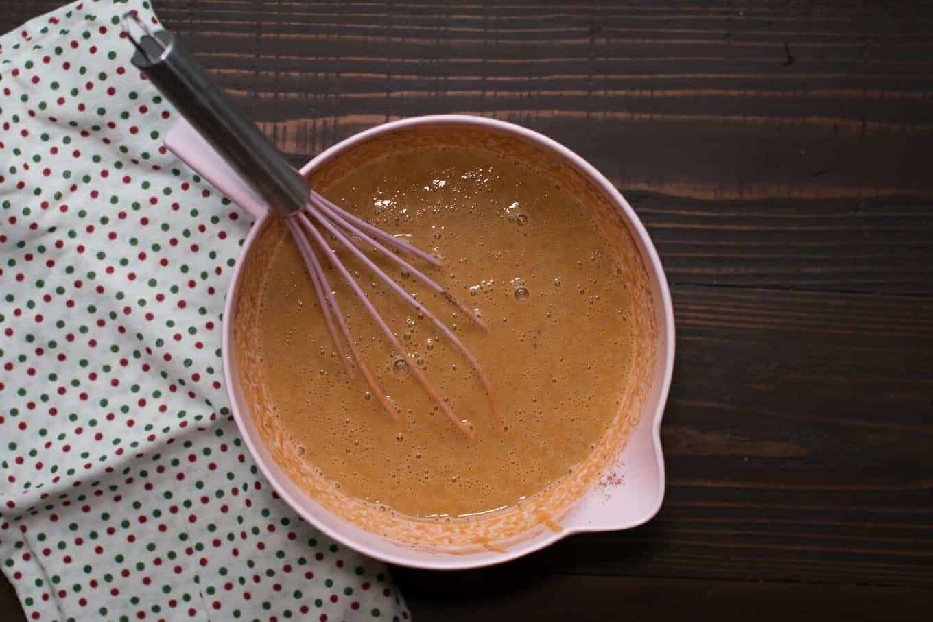 Torta di Zucca Senza Crosta allo Zucchero di Canna a Cottura Lenta 4 Ripieno di torta di zucca in una ciotola rosa con una frusta rosa all'interno.