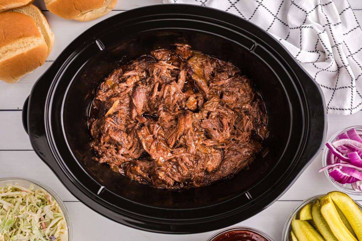 Manzo al Barbecue a Lenta Cottura 5 Manzo BBQ sfilacciato in una crockpot con sottaceti e coleslaw a lato.