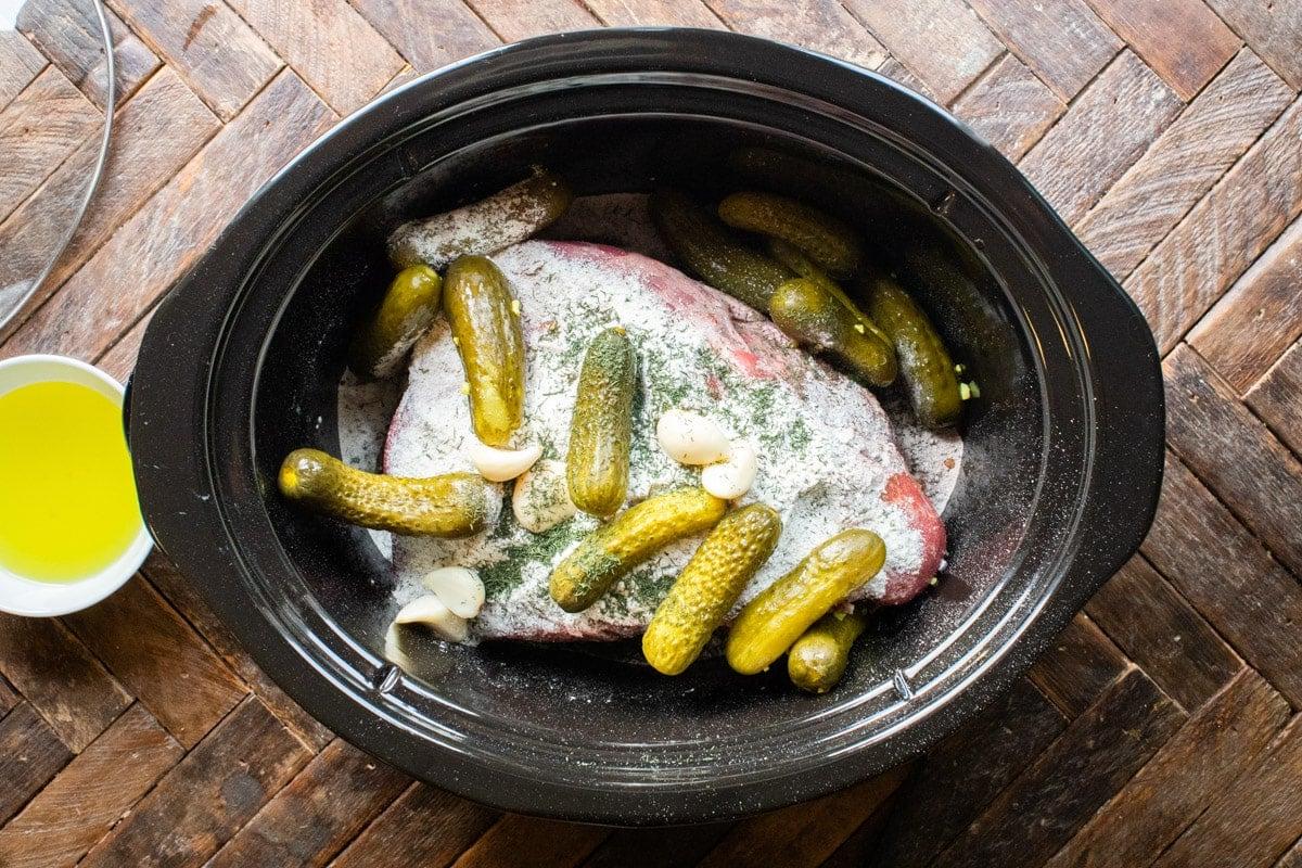 Spalla di manzo cruda ricoperta da condimenti e cetriolini sott'aceto, pronta per la cottura.