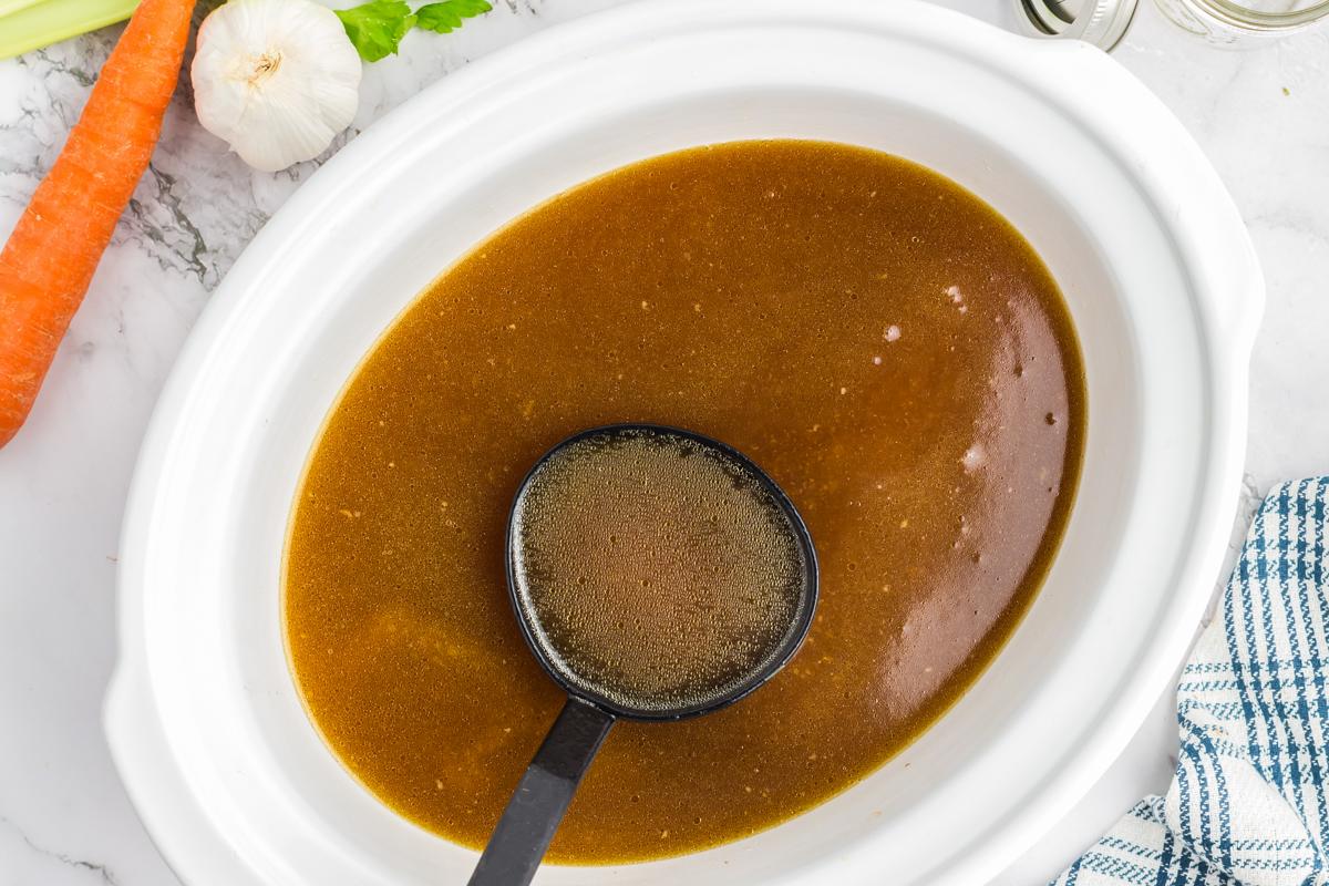 Brodo di Pollo a Cottura Lenta 5 Brodo di pollo caldo servito direttamente dalla slow cooker con un mestolo.