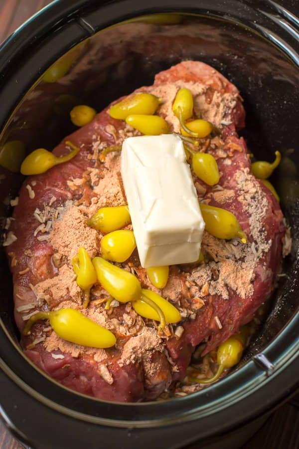 **Brasato Piccante alla Mississippi per Slow Cooker** 5 Primo piano di punta di petto di manzo cruda, peperoni piccanti e burro.