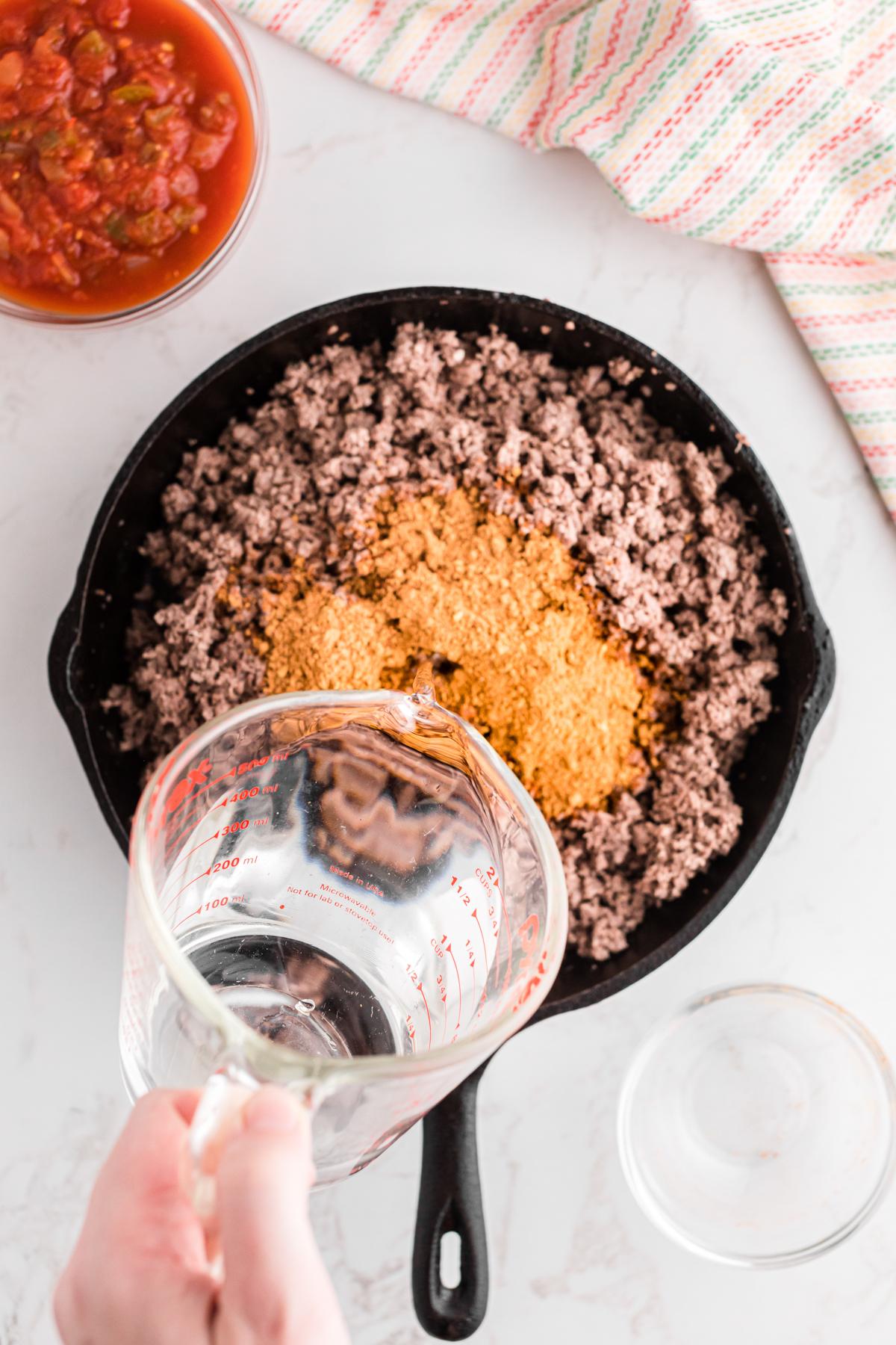 Salsa della Domenica Divertente 5 Condimento per taco e acqua aggiunti alla carne macinata in una padella.
