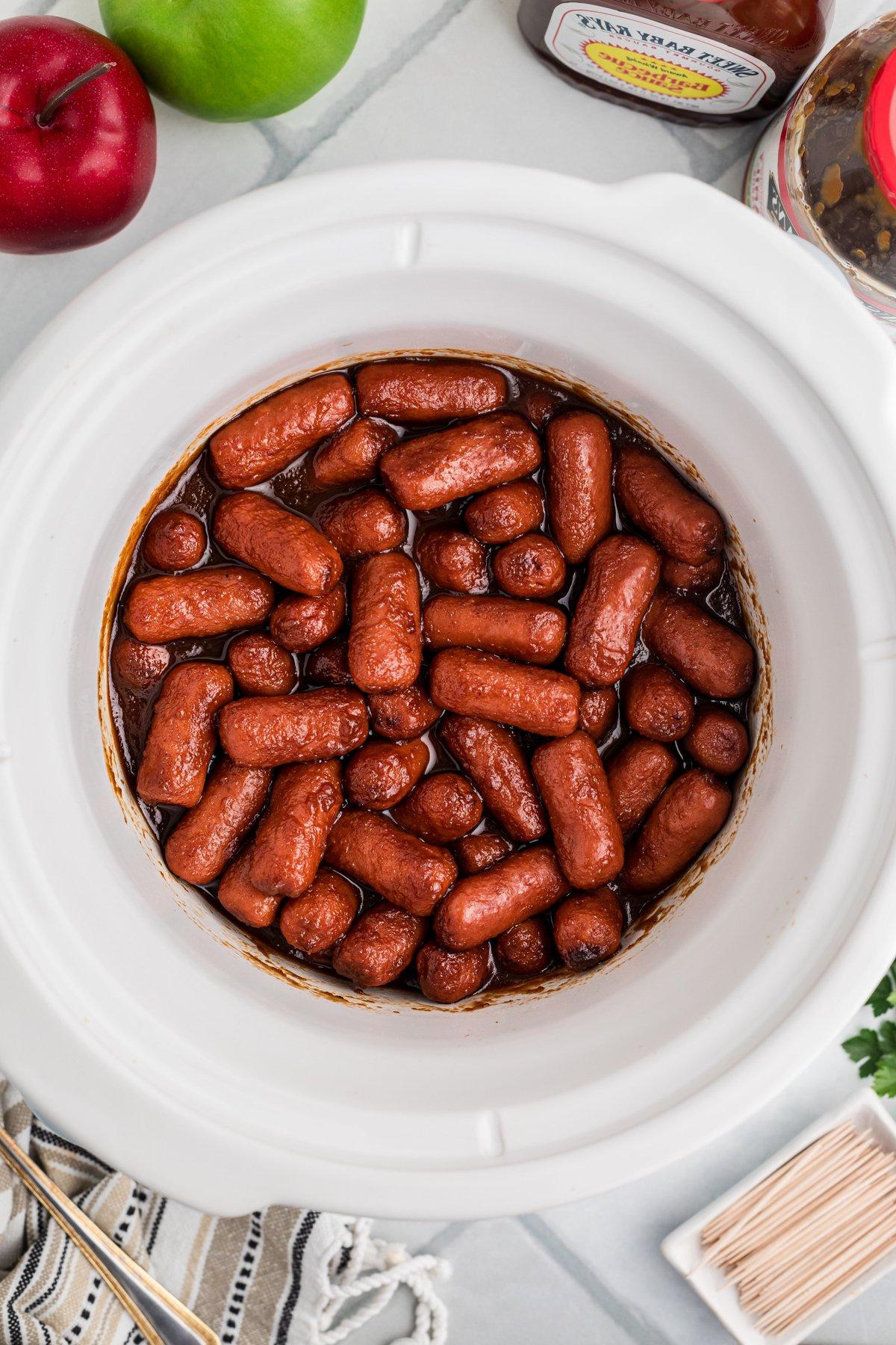 **Wurstel Piccoli al Burro di Mele in Slow Cooker** 5 Salsiccine mini al burro di mele in una slow cooker dopo aver completato la cottura, pronte da servire.