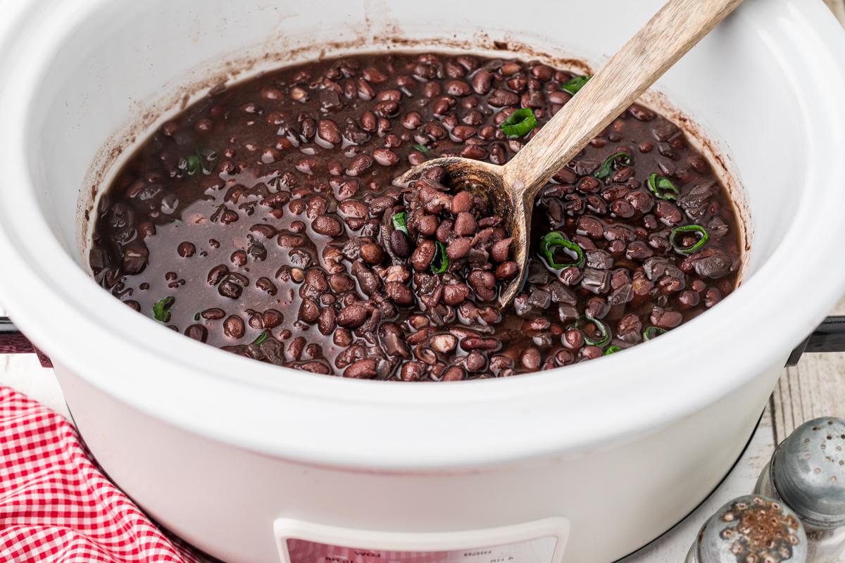 Fagioli Neri Cottura Lenta 5 Fagioli neri cotti e pronti per essere serviti in una slow cooker con un cucchiaio di legno.