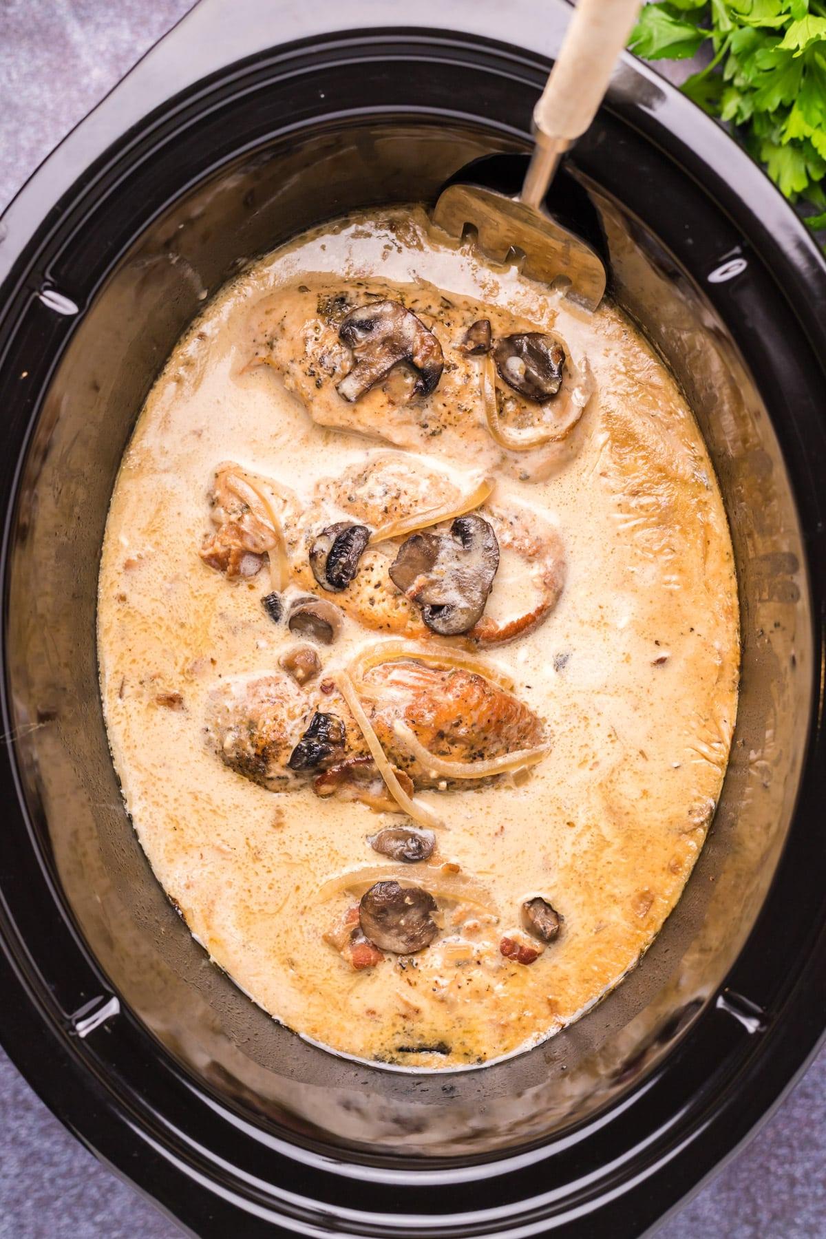 Pollo al Marsala in pentola a cottura lenta 5 Vista ravvicinata del pollo al Marsala nella slow cooker con un cucchiaio all'interno.
