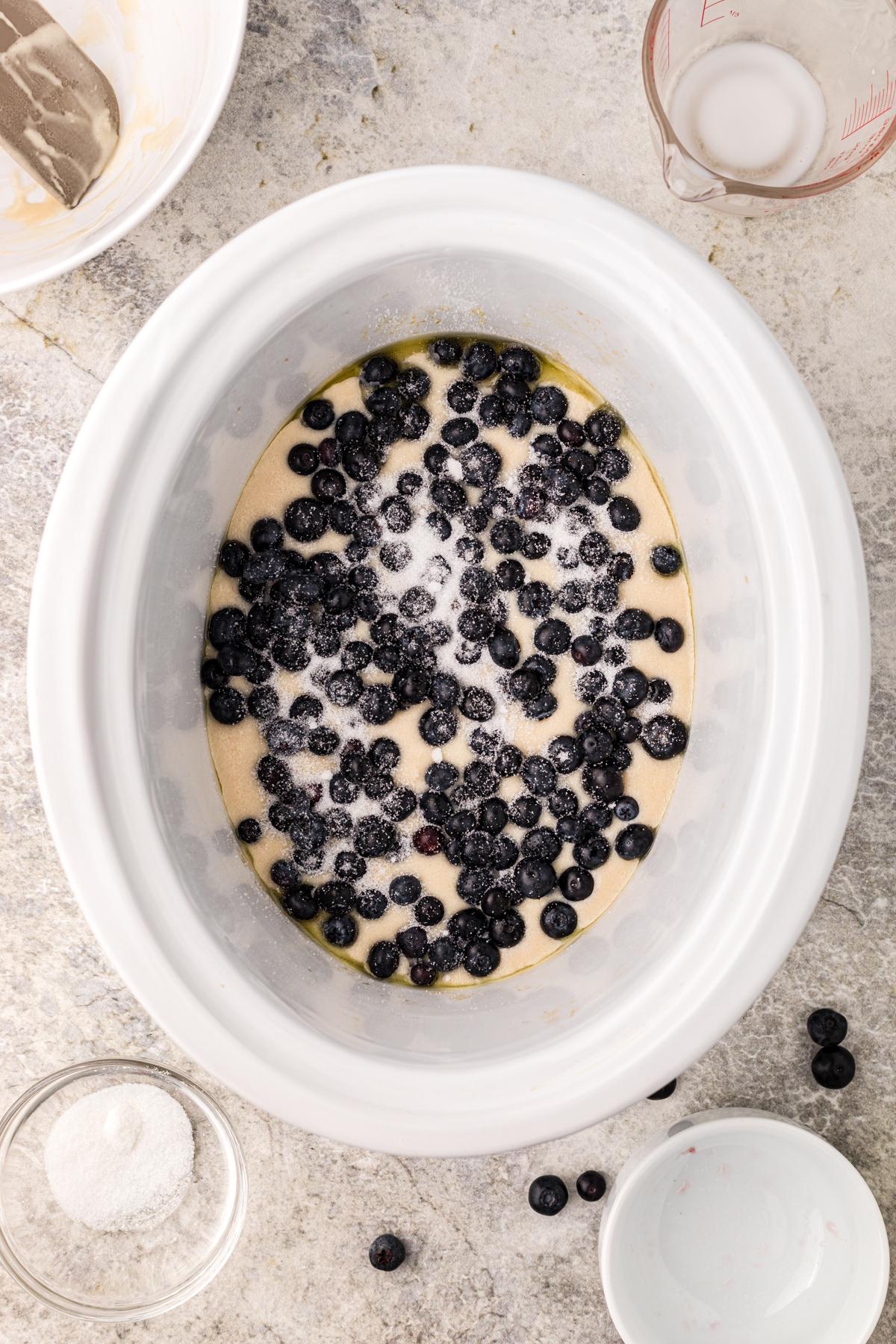 **Cobbler ai Mirtilli della Slow Cooker** 5 Zucchero cosparso sopra mirtilli e impasto del cobbler in un crockpot.