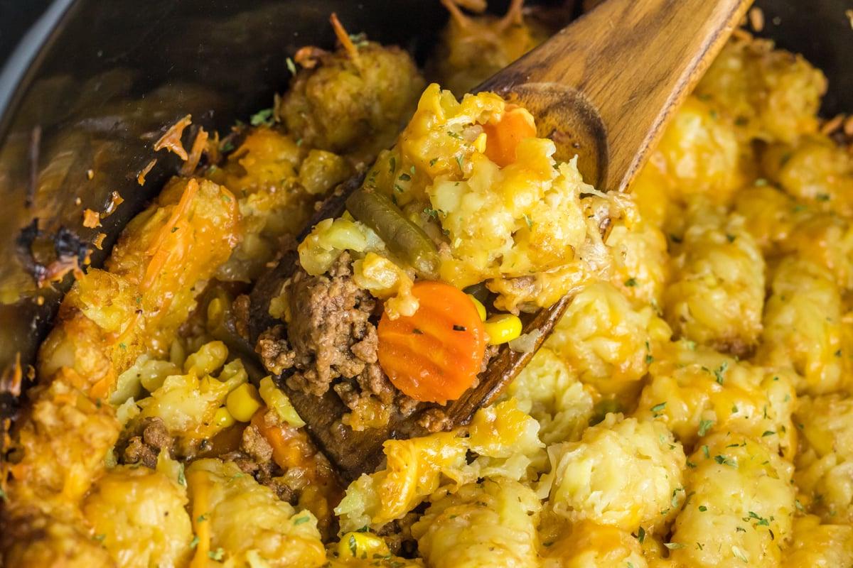 Sformato di Tater Tot alla Pastore 5 close up of shepherd's pie tater tot casserole on a wooden spoon in a crockpot.