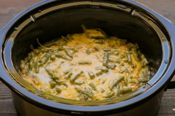 **Gratin di Fagiolini al Formaggio a Cottura Lenta** 5 Primo piano di una porzione di casseruola di fagiolini al formaggio, ancora nella slow cooker, mostrando la sua consistenza cremosa e il colore ricco prima dell'aggiunta finale delle cipolle croccanti.