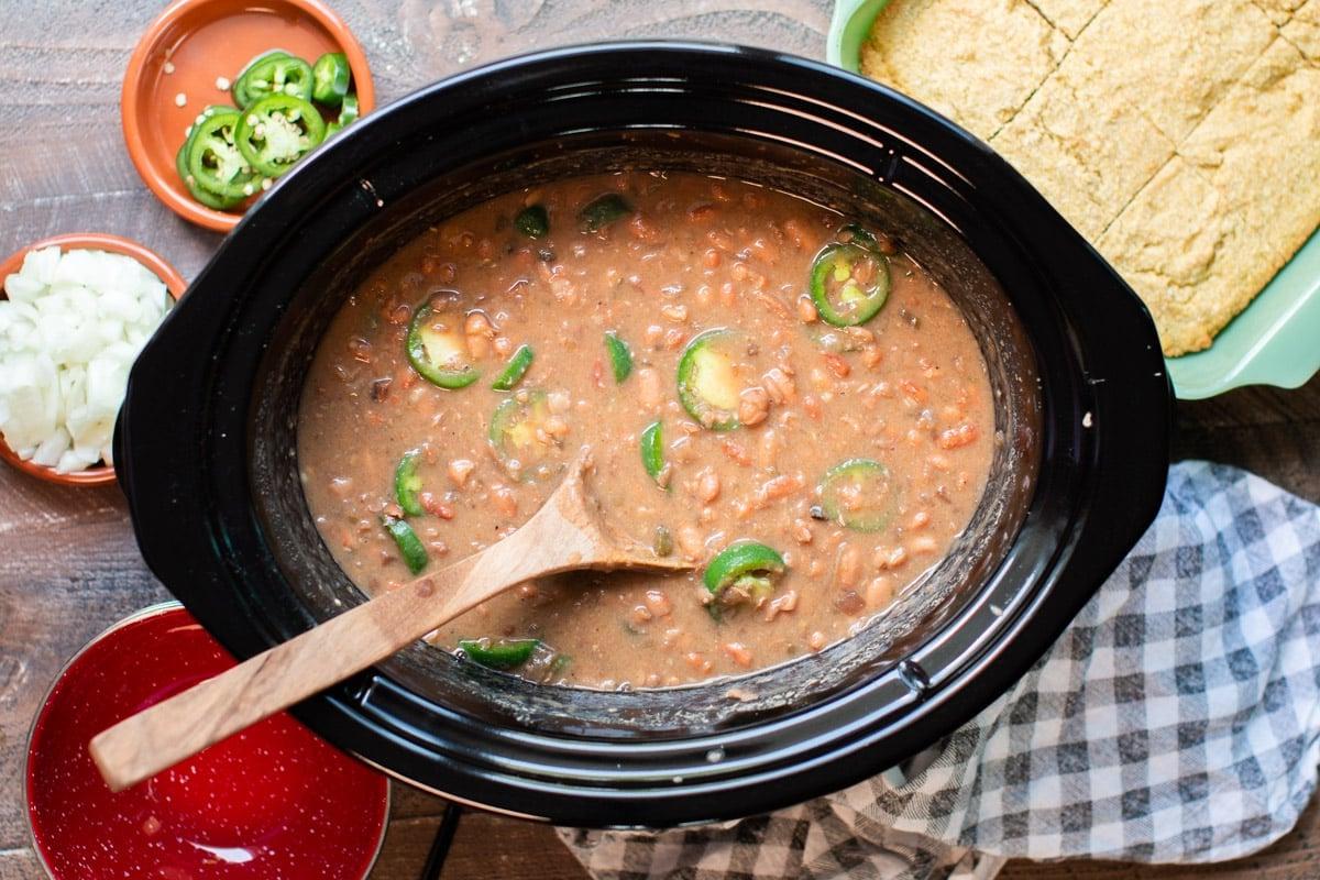 Fagioli Pinto Piccanti in Pentola a Cottura Lenta 6 Fagioli pinto cotti nella slow cooker con jalapeños e un mestolo di legno.