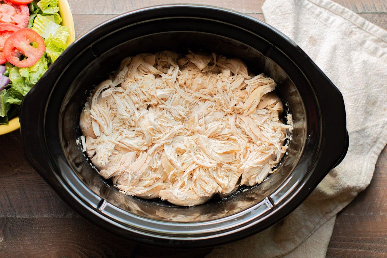 Pollo sfilacciato in slow cooker 6 Pentola a cottura lenta mezza piena di pollo sfilacciato di carne bianca.