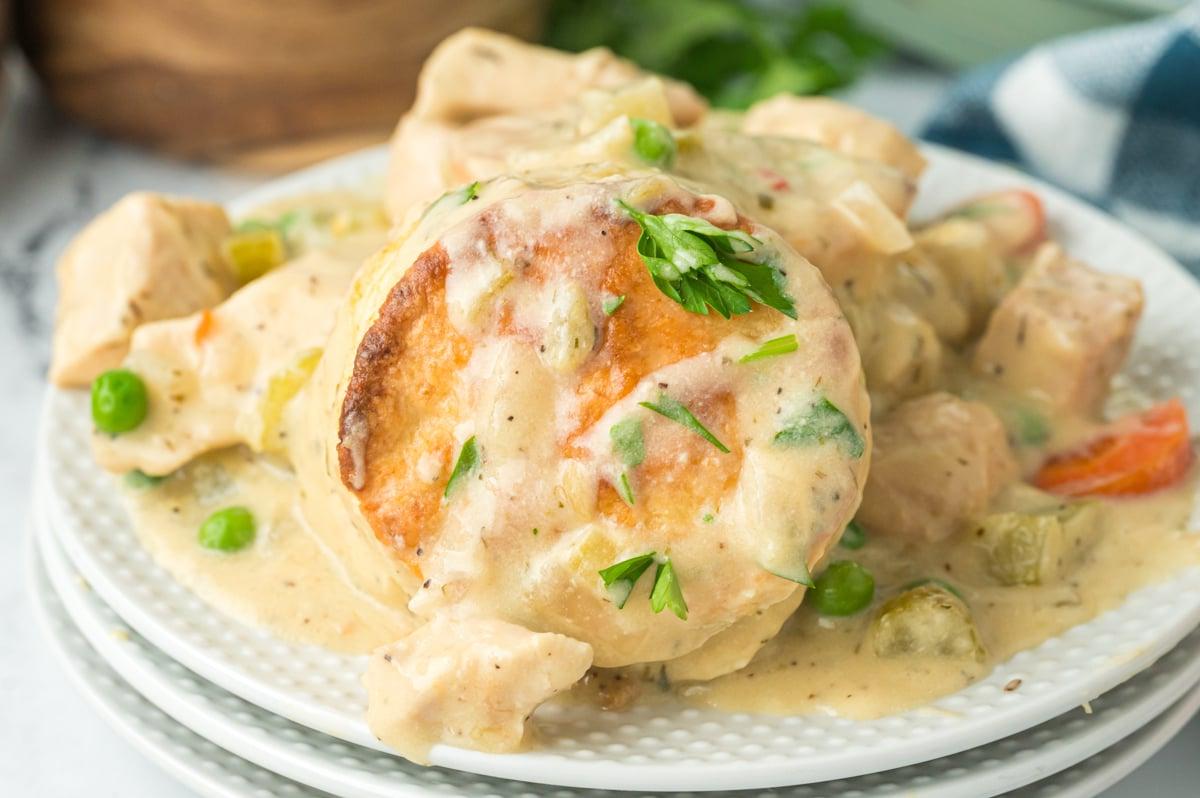 Facile Pasticcio di Pollo Cotto Lentamente con Focaccine 6 Una porzione di torta rustica di pollo in pentola a cottura lenta su una pila di piatti bianchi.