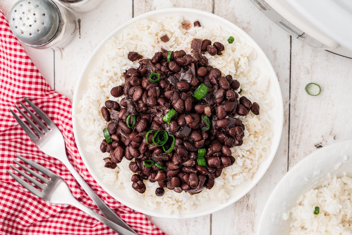 Fagioli Neri Cottura Lenta 6 Fagioli neri serviti su riso in un piatto in primo piano, con una slow cooker sullo sfondo.