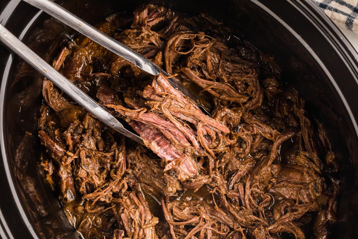Un paio di pinze che estraggono dell'arrosto di manzo della Georgia dalla slow cooker.
