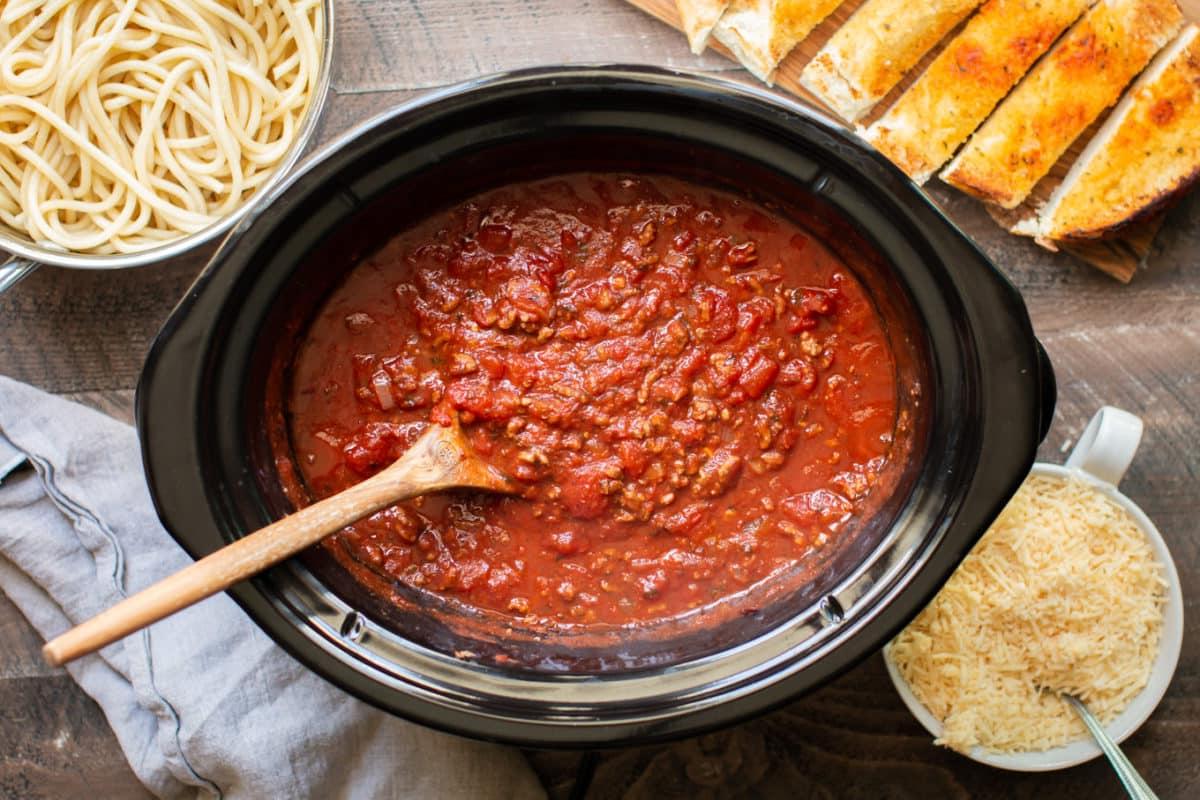 Sugo per Spaghetti a Cottura Lenta 6 Sugo cotto nella slow cooker con pane all'aglio e pasta sul lato.