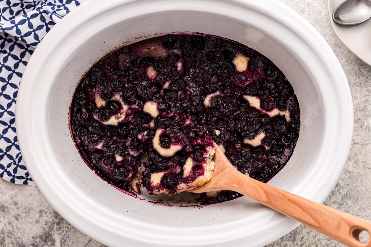 **Cobbler ai Mirtilli della Slow Cooker** 6 Cobbler di mirtilli al slow cooker con un cucchiaio di legno.
