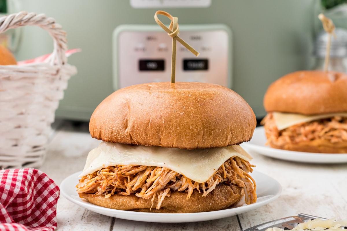 Panini al Pollo alla Parmigiana a Cottura Lenta 6 Panini di pollo alla parmigiana su piatti di portata accanto a una slow cooker.