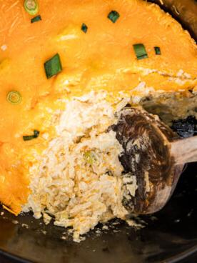 Patate per Feste in Slow Cooker 6 Un grande cucchiaio di legno che raccoglie una porzione di patate da festa cremosi dalla slow cooker.