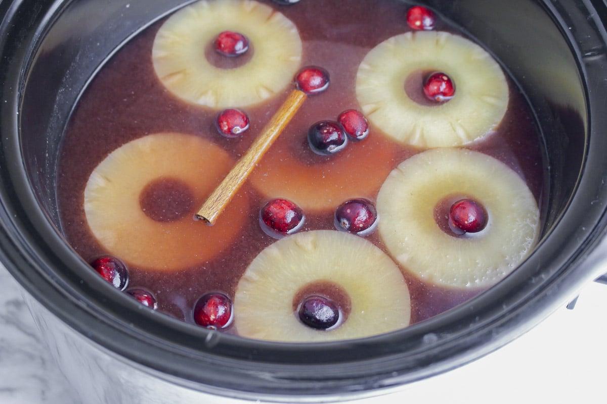 **Punch Piccante alla Cannella per Slow Cooker** 6 slow cooker con punch rosso caldo, ananas e stecche di cannella