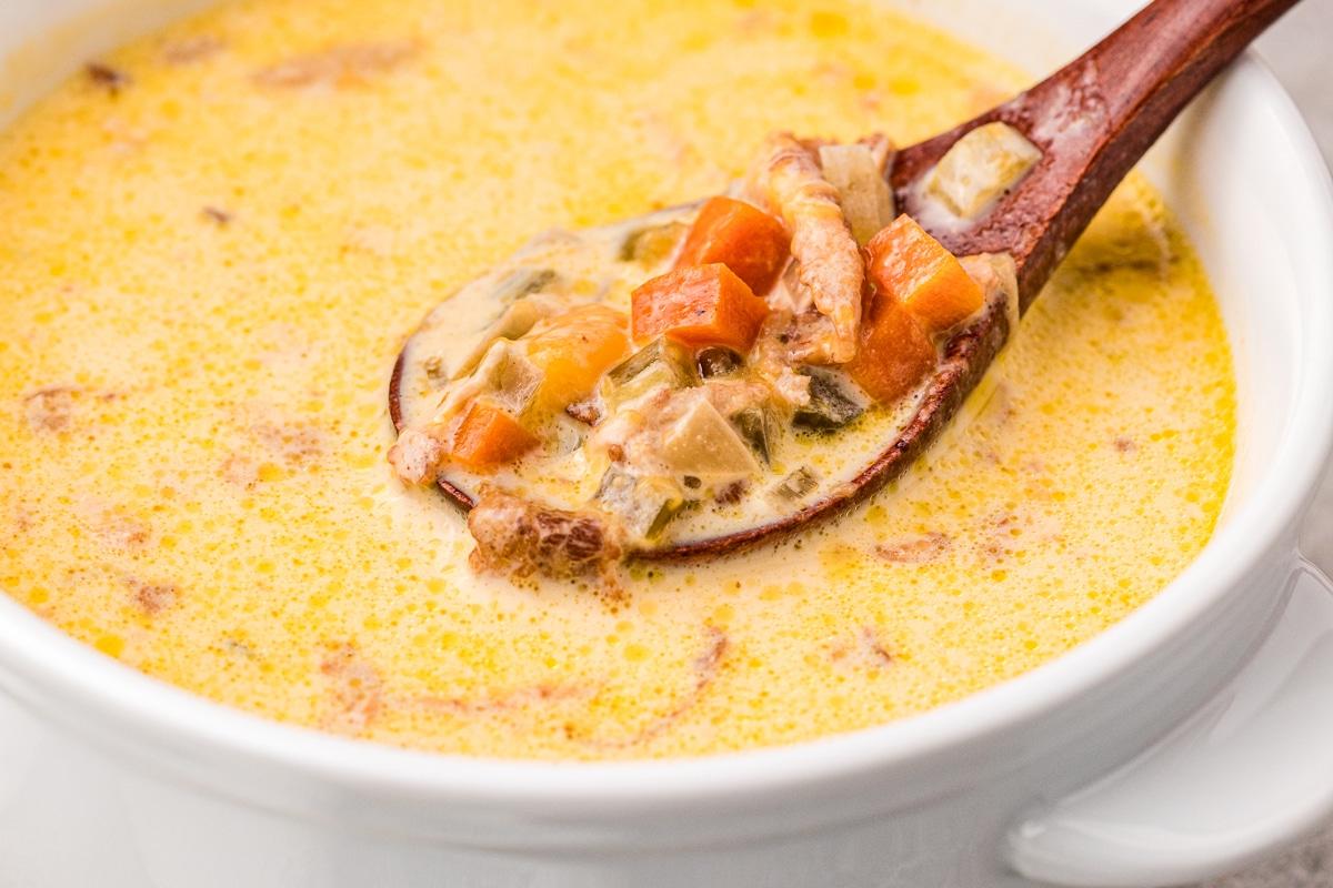 Zuppa alla birra e al formaggio 7 Primo piano di zuppa di formaggio e birra in una ciotola con un piccolo cucchiaio di legno.