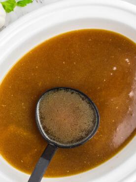 Brodo di Pollo a Cottura Lenta 7 Brodo di pollo nella slow cooker servito con un mestolo.