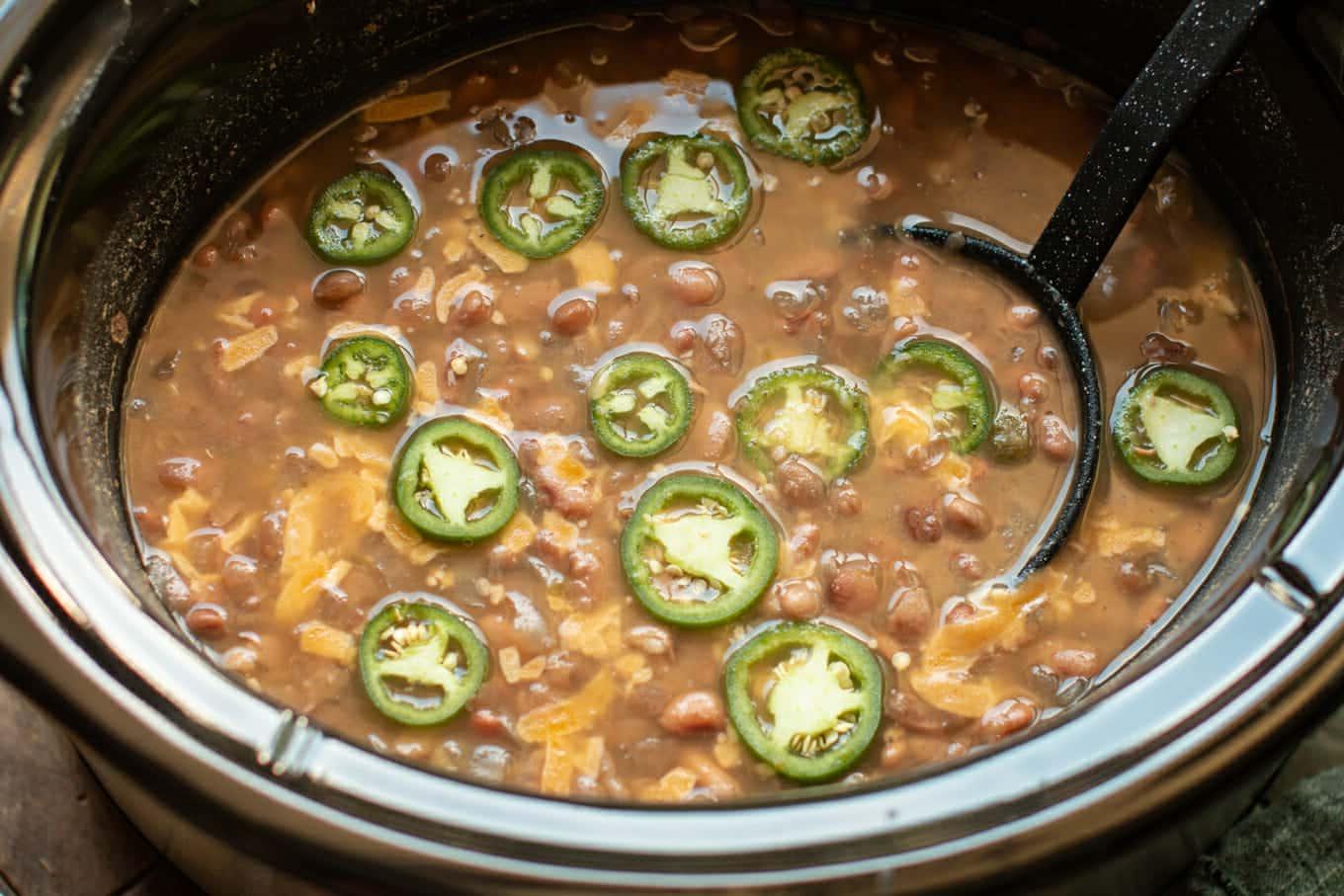 Fagioli Pinto Piccanti in Pentola a Cottura Lenta 7 Primo piano di fagioli pinto con un mestolo e jalapeños sopra.