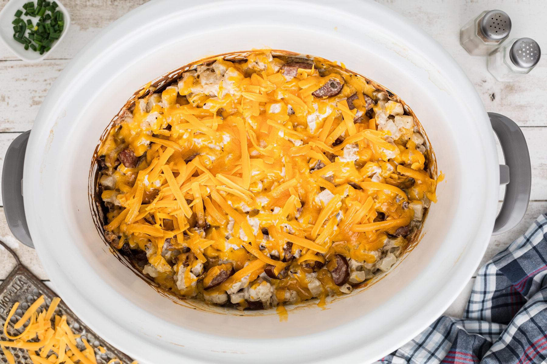Sformato di Kielbasa e Hashbrowns in Cottura Lenta 7 Formaggio Cheddar aggiunto sopra gli ingredienti nella slow cooker.